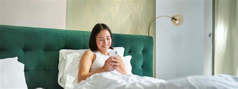S Es Koreanisches M Dchen Im Bett Das Smartphone In Der Hand H Lt Und