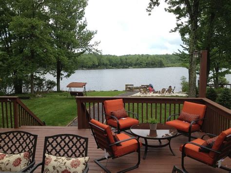 An Outdoor Deck With Four Chairs And A Table On It Overlooking A Lake In The Background