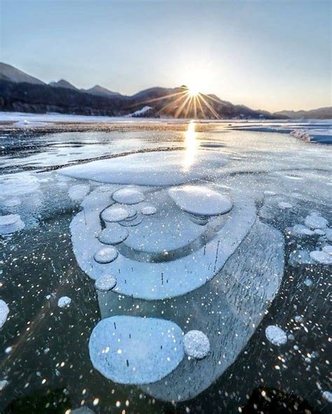 The Sun Is Shining Over An Icy Lake With Ice Flakes And Bubbles On It