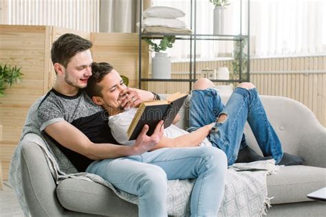 Attractive Gay Couple Reading Book On The Sofa At Home In Living Room Stock Image Image Of