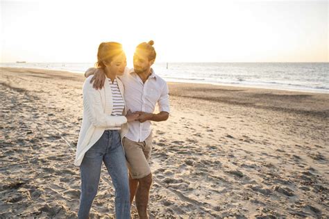 Young Couple Holding Hands While Walking At Beach During Sunny Day