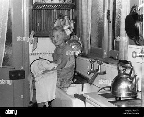 Young Girl Sitting On The Kitchen Worktop Drying Dishes After Doing The Washing Up Circa 1945