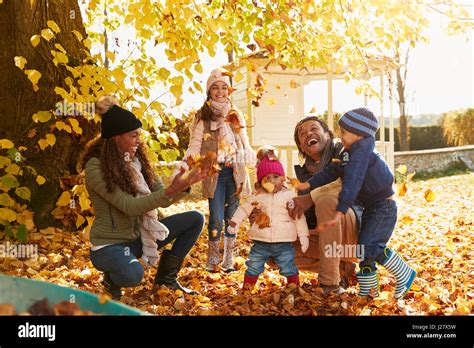 Children Helping Parents To Collect Autumn Leaves In Garden Stock Photo