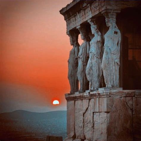 The Sun Is Setting Behind Some Statues On Top Of A Building With