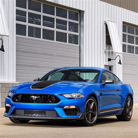 A Blue Ford Mustang Parked In Front Of A White Building With Garage