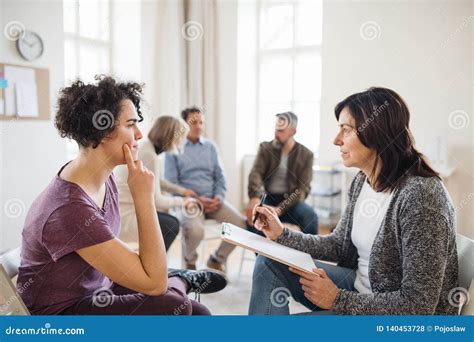 Senior Counselor With Clipboard Talking To A Woman During Group Therapy