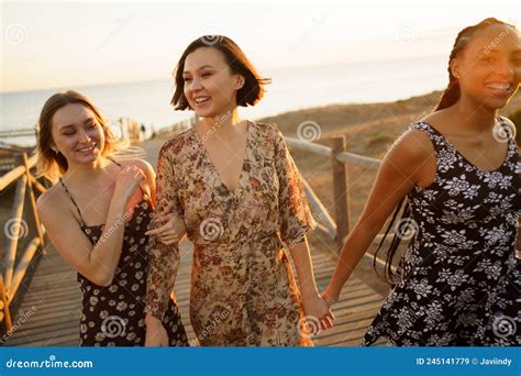 Content Multiethnic Girlfriends Walking On Footbridge On Seashore Stock