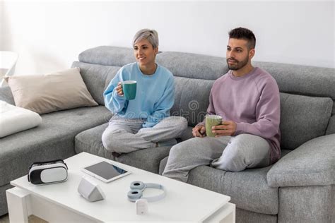 Young Couple Cuddling On A Sofa And Drinking Coffee While Watching Tv