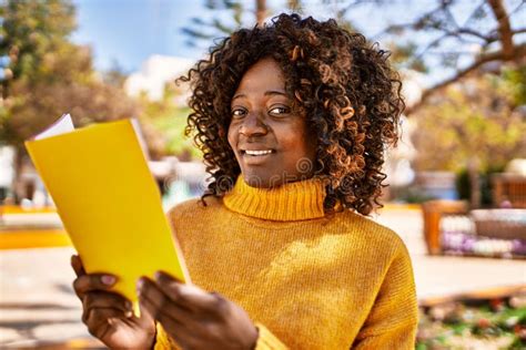 African American Woman Smiling Confident Reading Book At Park Stock