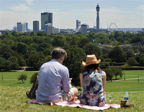 People Bask In The Sun On Primrose Hill North London Backdropped By A View Of The City Of