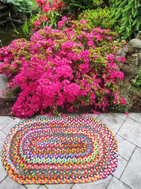 A Colorful Rug In The Middle Of A Garden With Pink Flowers And A Buddha