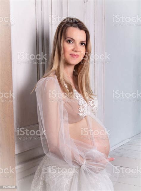 Pregnant Blonde Woman In White Clothes Holding Her Hands On Her Stomach