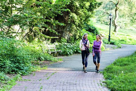 Female Friends Talking While Walking On Footpath At Park Stock Photo