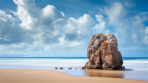 Big Rock Stone On Beach Sand Ocean Waves Under Blue Clouds