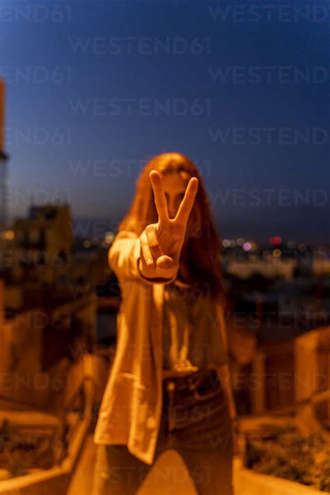 Young Woman Doing Peace Sign At Blue Hour Stock Photo