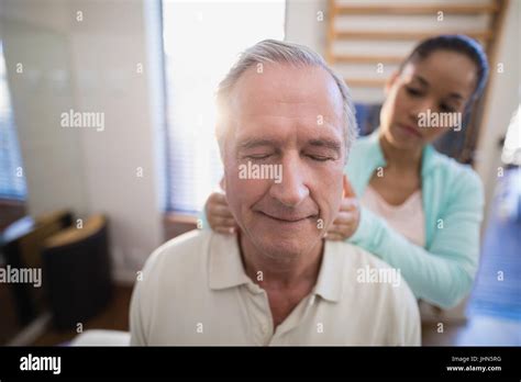 Senior Male Patient With Eyes Closed Receiving Neck Massage From Female Therapist At Hospital
