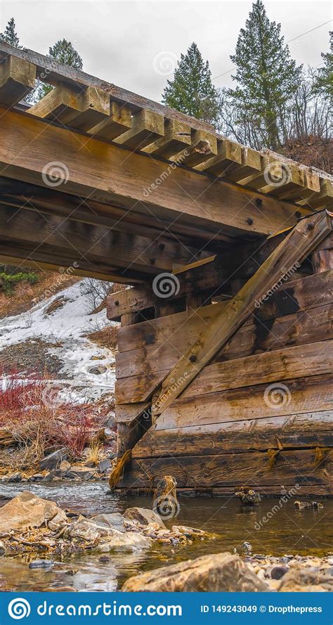 Vertical Rustic Wooden Bridge Crossing Over A Rocky Stream With Clear