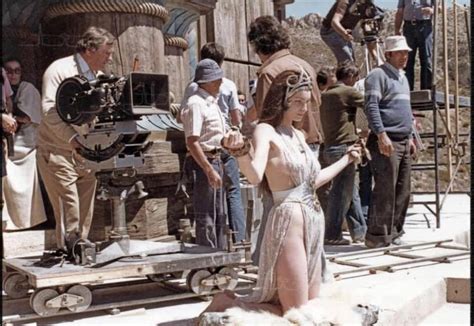 A Woman In A White Dress Standing Next To A Group Of People On A Set