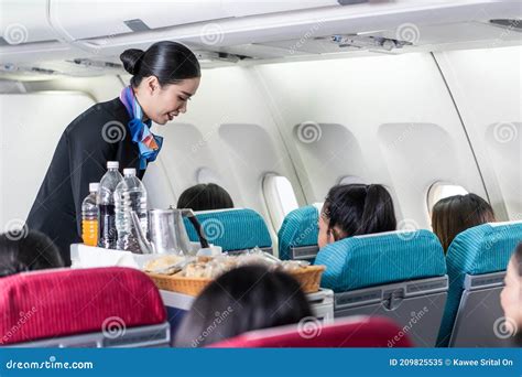 Asian Female Flight Attendant Serving Food And Drink To Passengers On