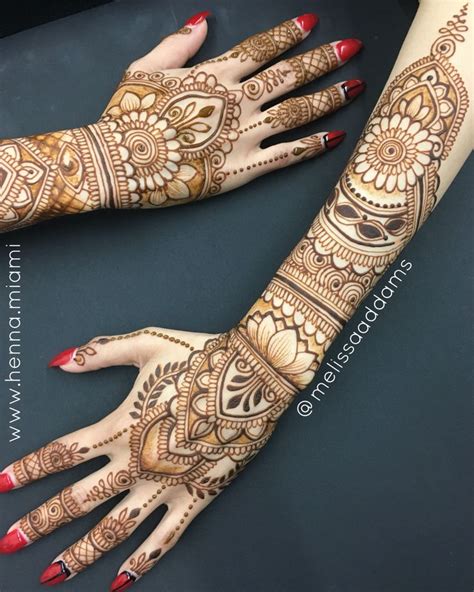two hands with henna tattoos on them and red nails one is holding the other hand