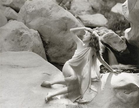 A Black And White Photo Of A Woman Sitting On Rocks With Her Hair Blowing In The Wind