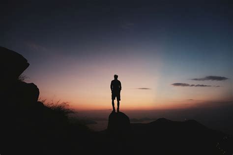 Rear View Of Silhouette Man Standing On Cliff Against Sky During Sunset