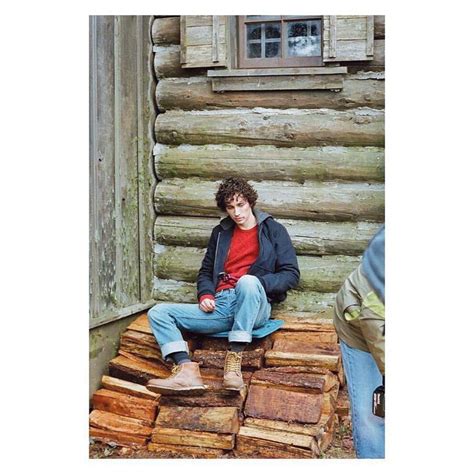 A Man Sitting On Top Of A Pile Of Wood Next To A Log Cabin Window