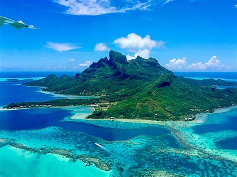 An Airplane Wing Flying Over A Small Island In The Middle Of The Ocean