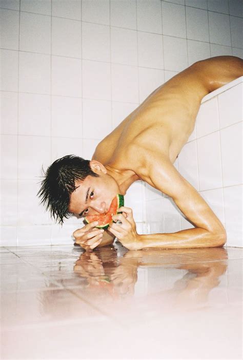 A Naked Man Eating A Slice Of Watermelon In The Bathtub With White Tiles On The Wall Behind Him
