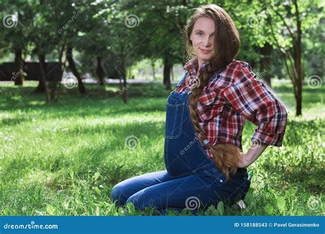 Beautiful Pregnant Woman In Denim Overalls Sitting On The Grass In The Park Stock Image Image
