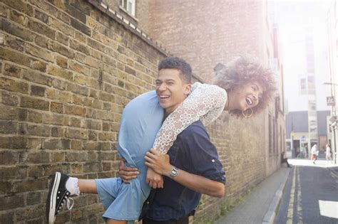 Young Couple Fooling Around In Street Man Carrying Woman Over Shoulder
