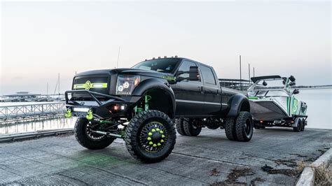 Two Large Trucks Are Parked On The Side Of The Road By The Water And Dock