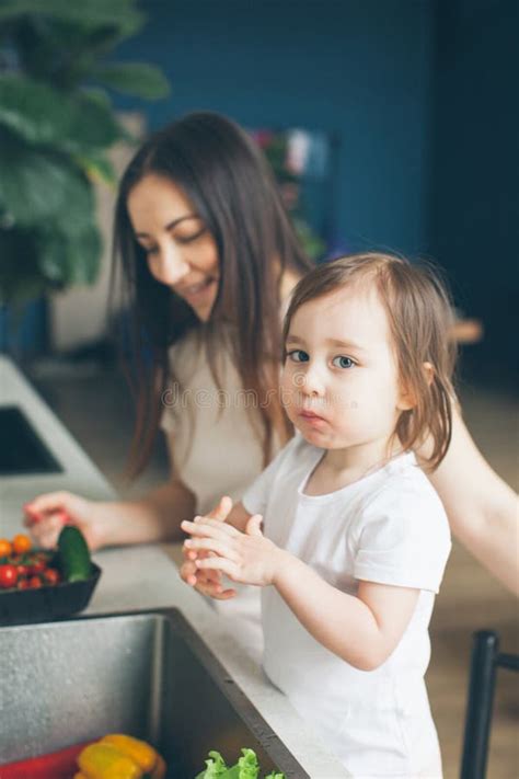 Mom And Two Year Old Daughter Wash Vegetables In The Kitchen Sink Side View Stock Image