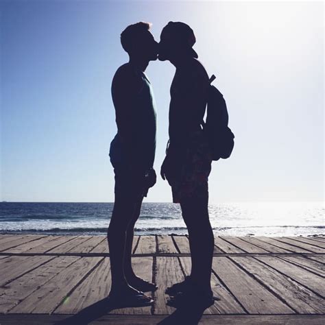 Two People Standing On A Pier Kissing Each Other With The Sun Shining In The Background