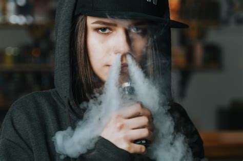 Premium Photo Young Pretty Woman In Cap Smoke An Electronic Cigarette At The Vape Shop Hip