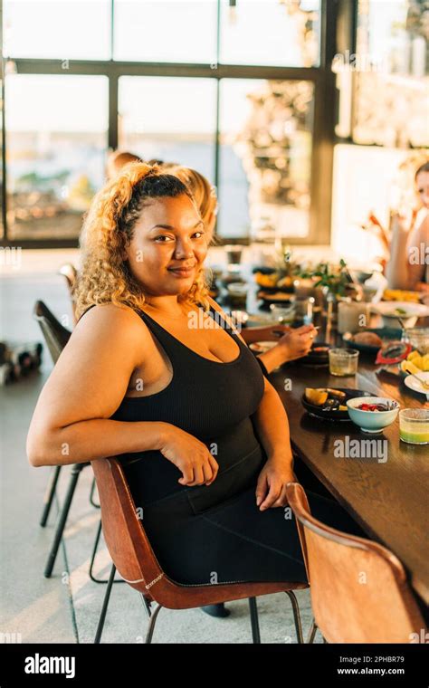 Portrait Of Smiling Plus Size Woman Sitting On Chair With Breakfast At