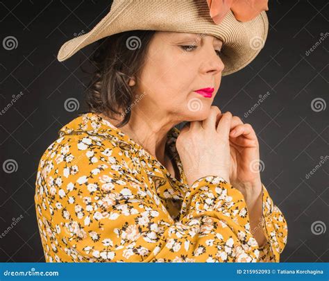 Portrait Of A Pensive Mature Woman In A Straw Hat And Yellow Dress With