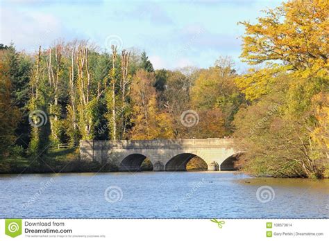 Stone Bridge Over A Lake In The Autumn Sunshine With Tree Leaves Stock