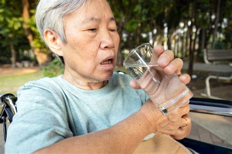 Asian Senior Woman Holding Glass Of Waterhands Shaking While Drinking