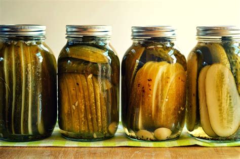 Four Jars Filled With Pickles Sitting On Top Of A Table