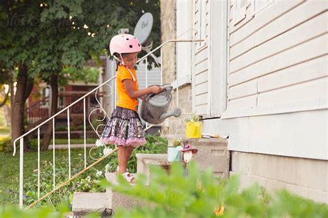 Pretty Child In A Pink Helmet Watering Some Flowers By Stocksy