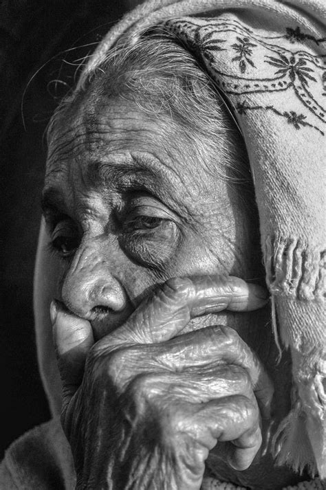 An Old Woman Wearing A Head Scarf And Holding Her Hand To Her Face With Both Hands
