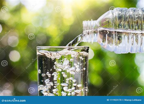 Drinking Water Pouring From Bottle Into Glass On Blurred Fresh Green
