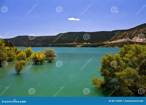 Yellow Trees In Turquoise Artificial Lake In Blue Sky In Summertime