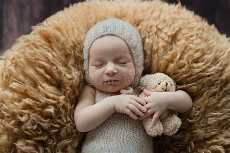 Cute Newborn Baby Sleeping On Brown Fur Blanket With Stuffed Teddy Bear