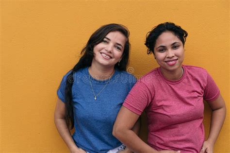 Latin Lesbian Couple Standing On A Yellow Wall Stock Image Image Of