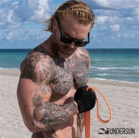 A Man With Tattoos On His Chest Holding An Orange Frisbee At The Beach