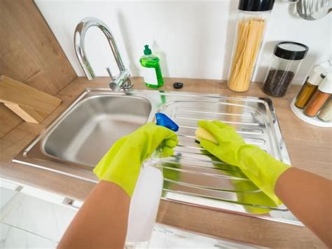 A Person In Yellow Gloves Cleaning A Kitchen Sink With A Rag And