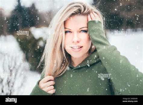 beautiful attractive blonde outdoor portrait in winter in snowfall wearing a hoodie stock