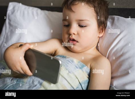 Smart Cute Boy Holding Phone Lying On The Bed In Morning Stock Photo